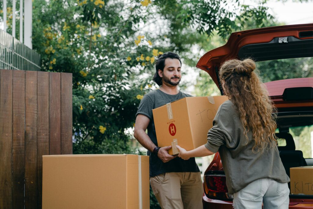 Relocation Assistance Boyfriend and girlfriend in casual wear helping each other with unpacking car while moving in together on sunny summer day