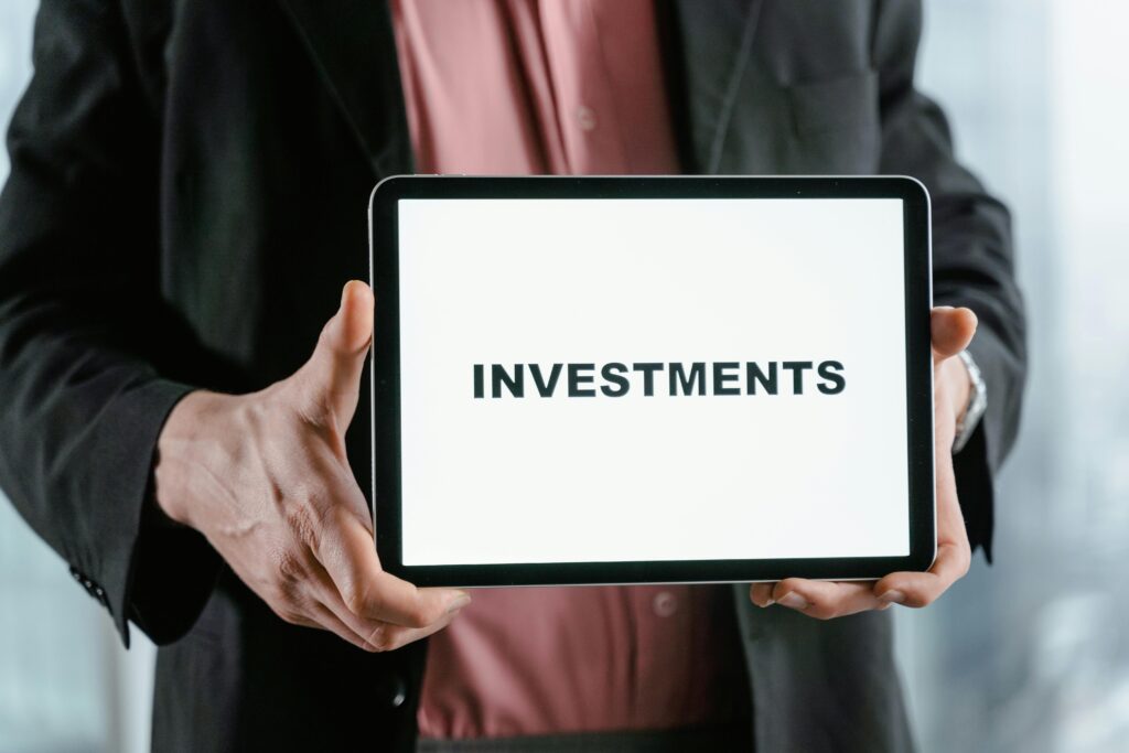 Investment Analysis A businessman in a suit holds a tablet displaying the text 'INVESTMENTS'.