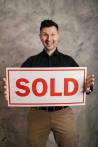 Best realtor in Yorba Linda Cheerful real estate agent holding a sold sign, indoors, symbolizing success in property sales.