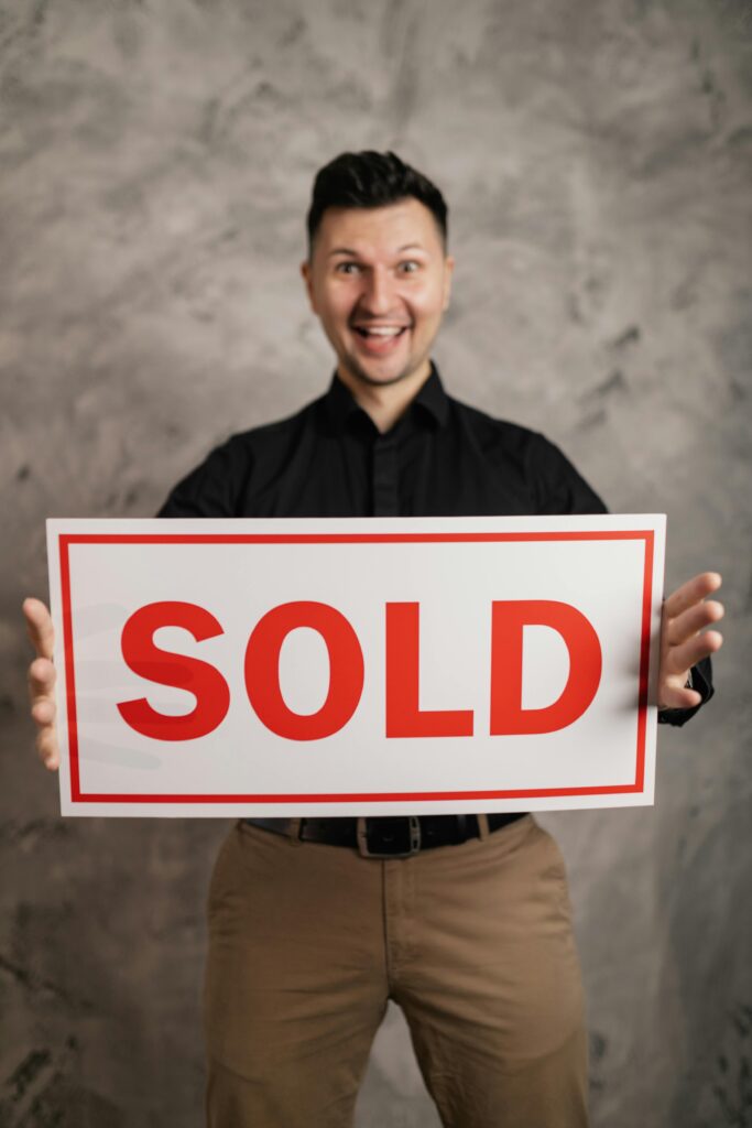 Best realtor in Yorba Linda Cheerful real estate agent holding a sold sign, indoors, symbolizing success in property sales.