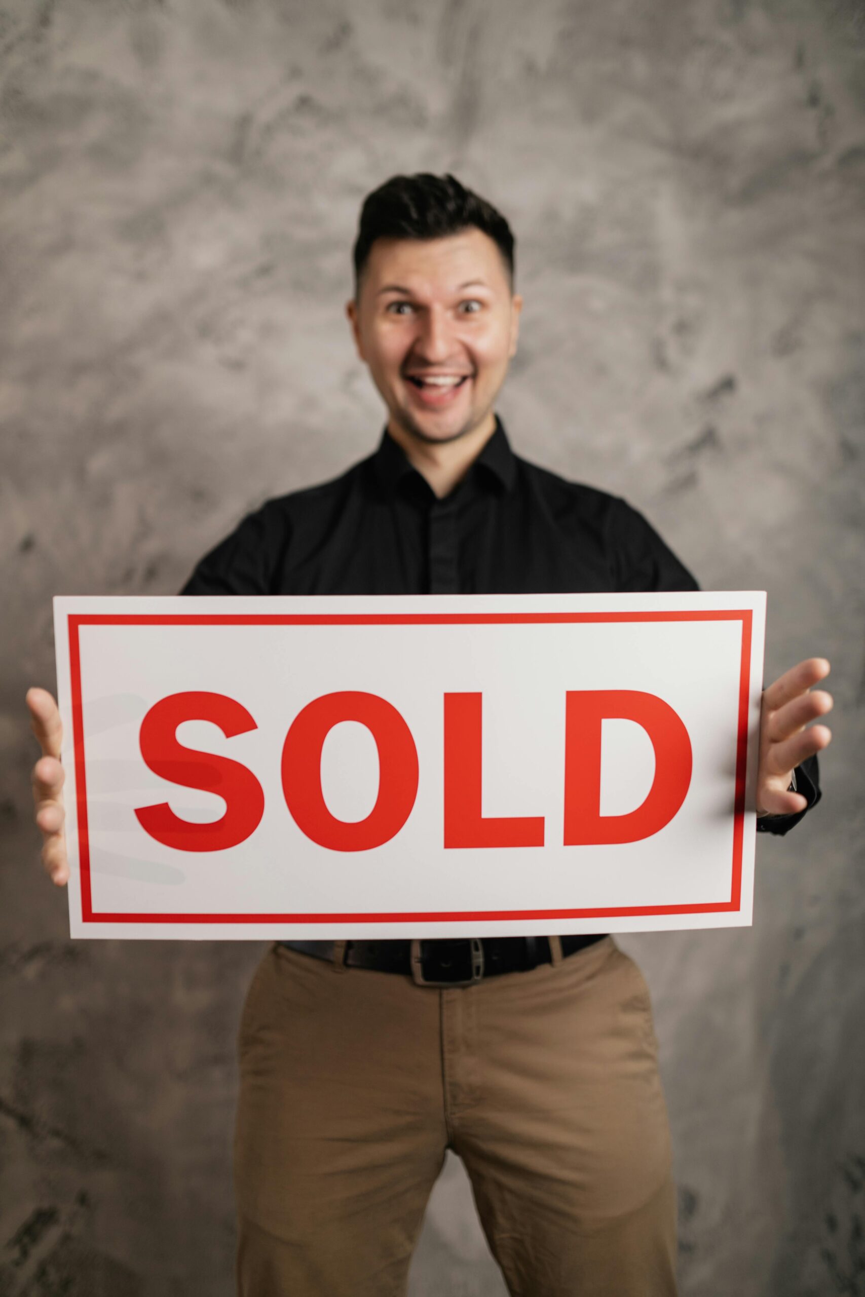 Cheerful real estate agent holding a sold sign, indoors, symbolizing success in property sales.